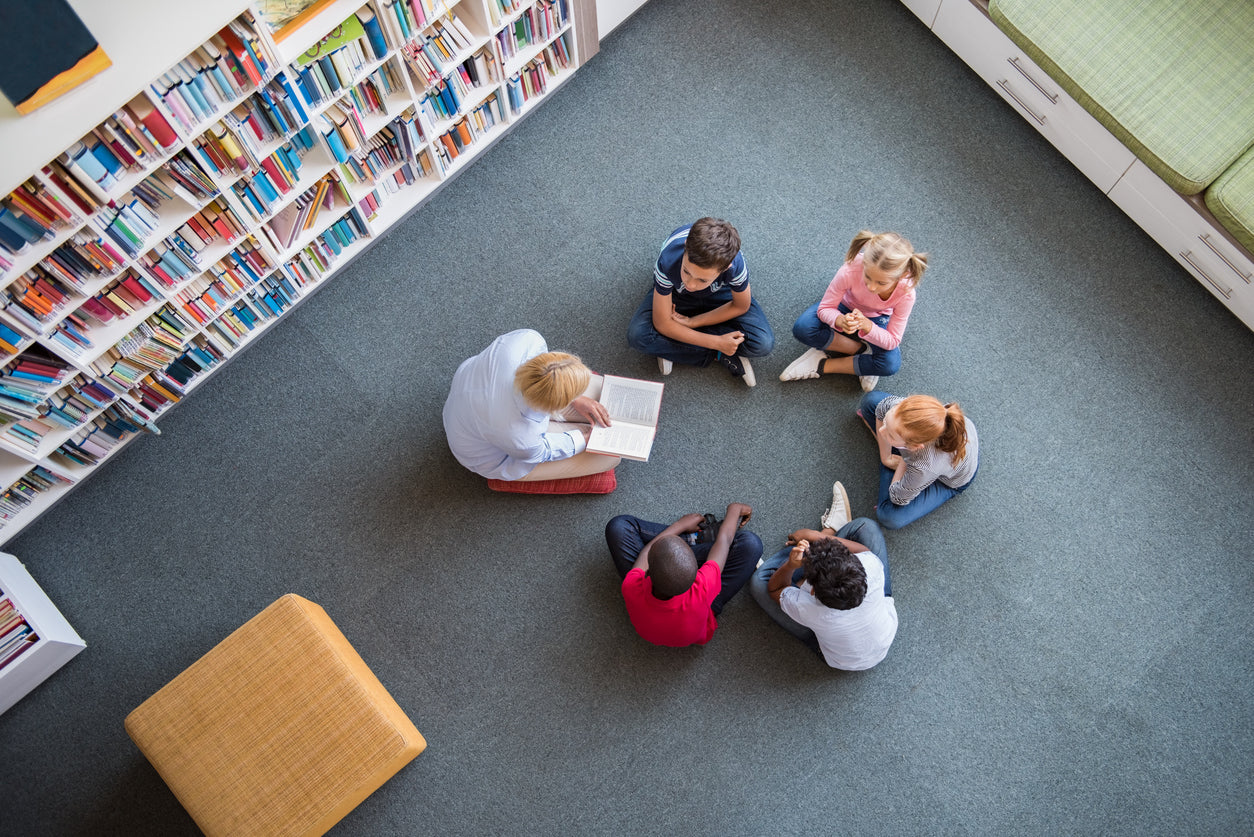 students sitting on the floor of the classroom library reading