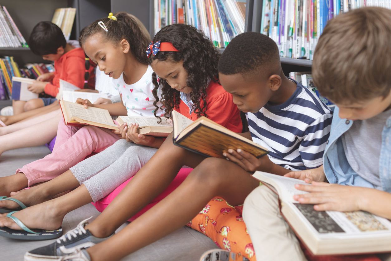 young students sitting on the floor of the library reading