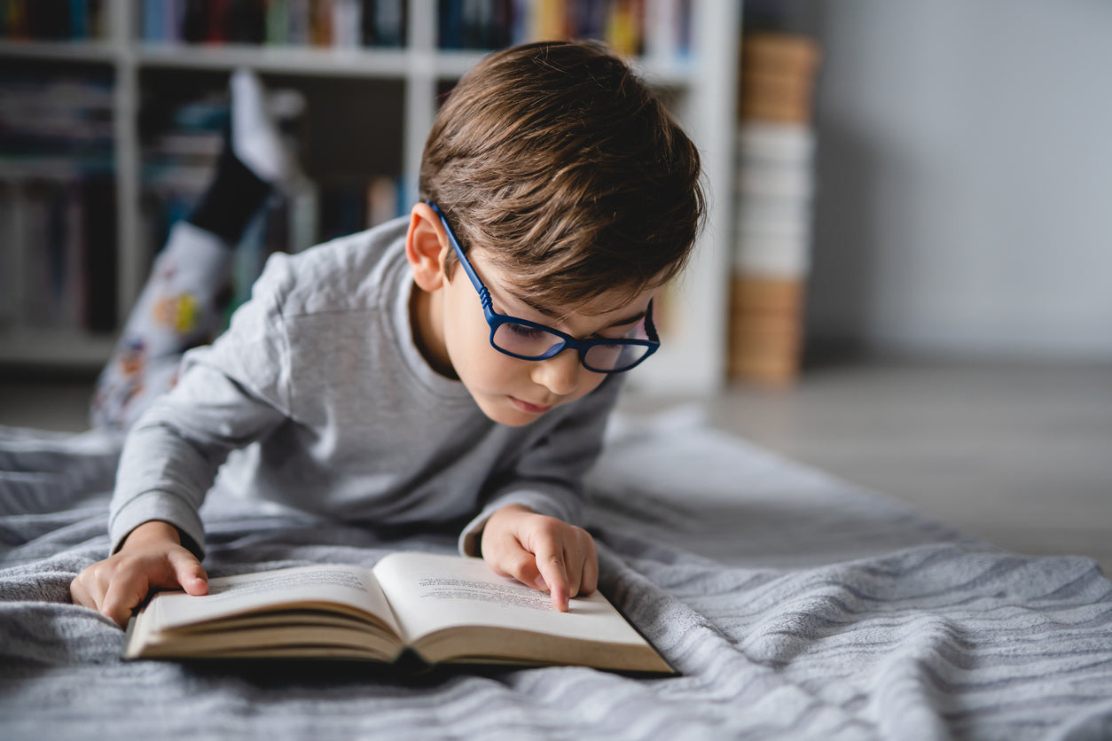 young boy reading a book on the floor is his room
