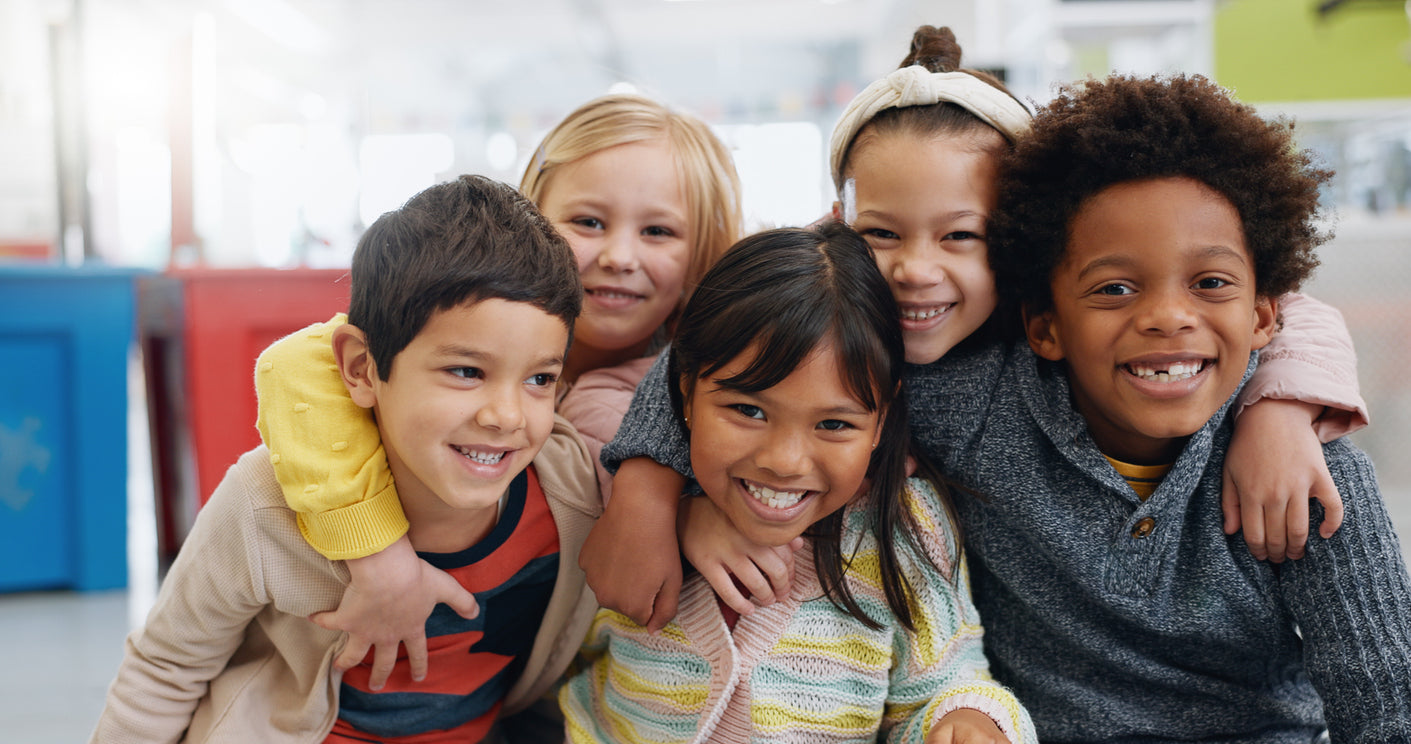 group of elementary school students smiling with their arms around eachother's shoulders.