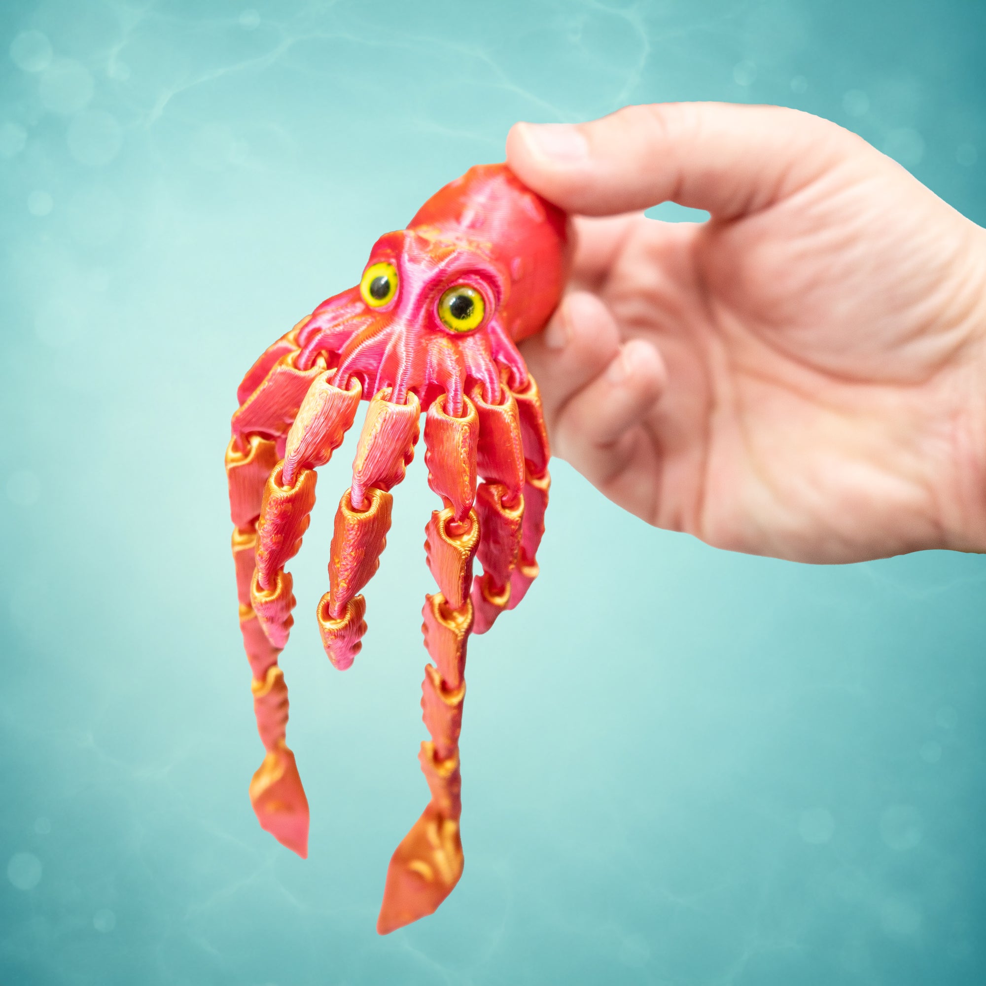 Orange and pink 3D-printed squid fidget toy held in a hand against an aqua underwater background.