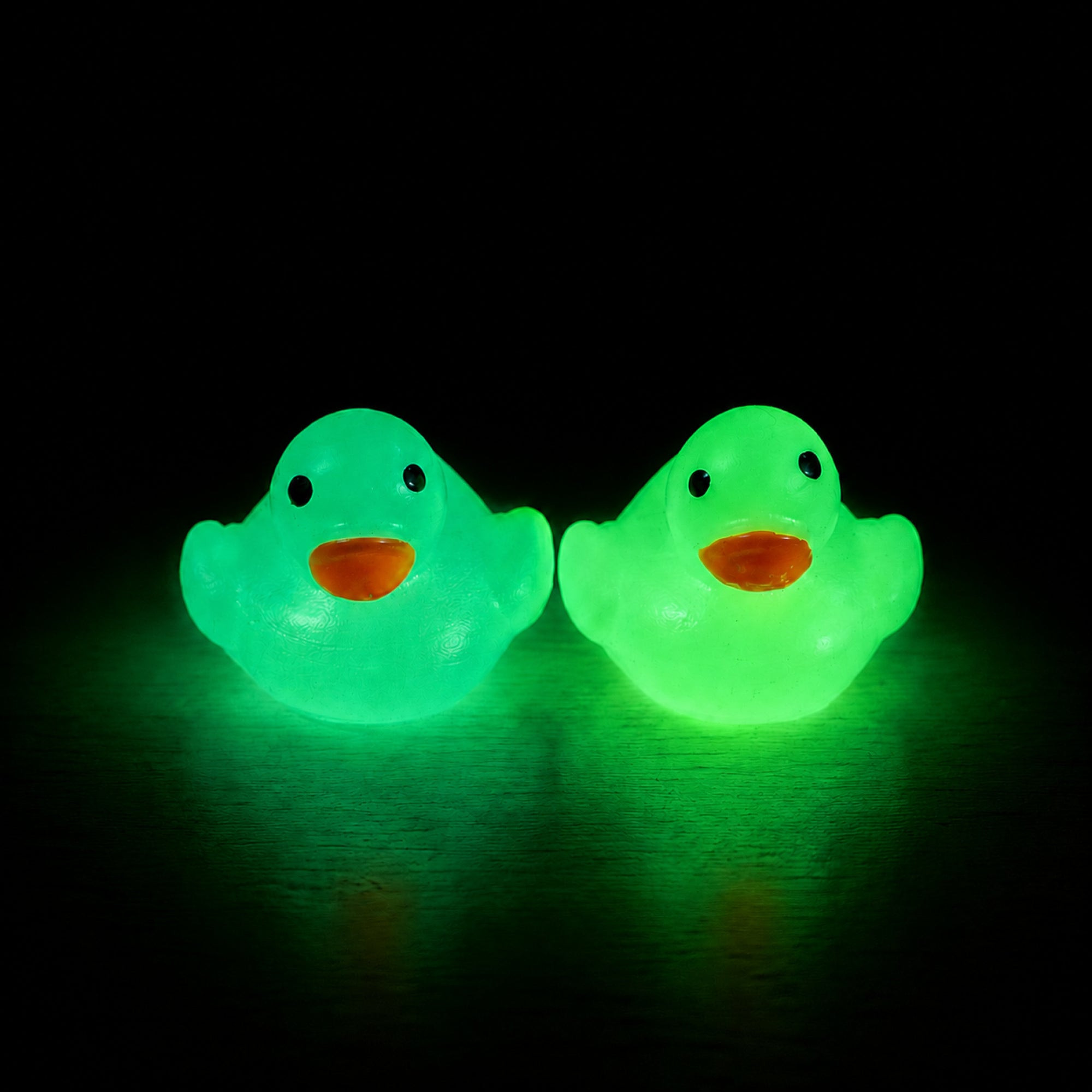 Two Scented Glow-in-the-Dark Squishy Mini Ducks glowing green against a black background.